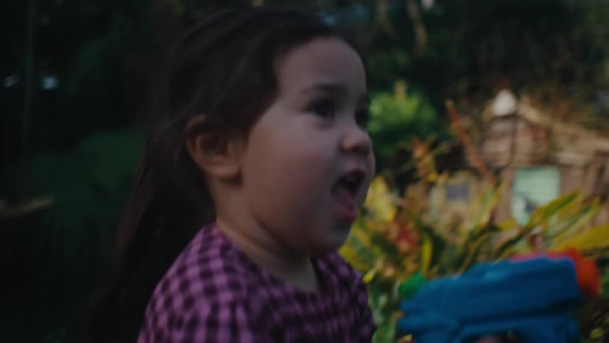Little girl playing in the backyard in a garden with a toy gun that sprays water