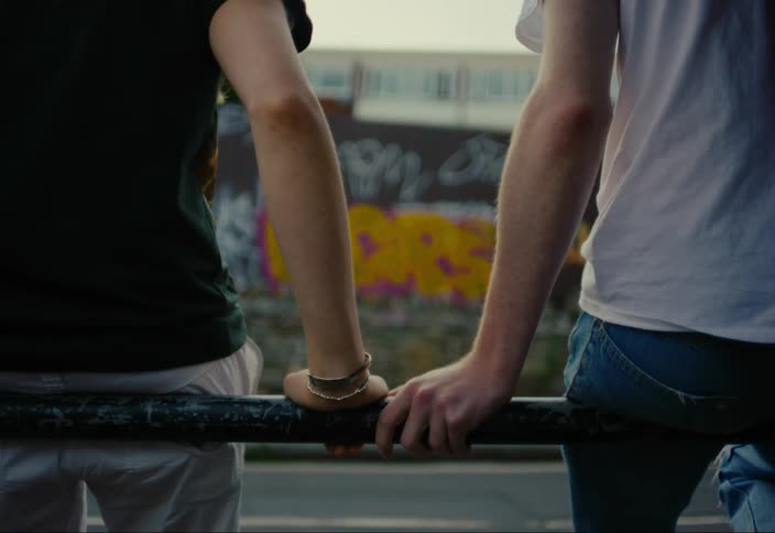 Two people sitting leaning on a railing holding hands in a romantic way