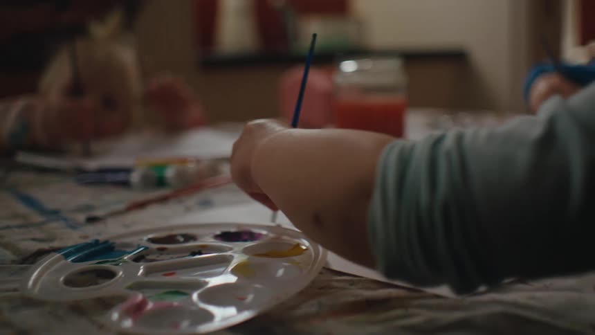 Three small children sitting at a table painting with paint