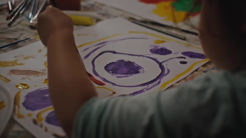 A little girls hand using a paintbrush to paint a paper with abstract designs
