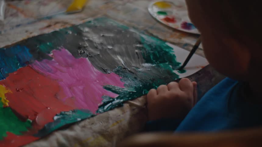 A child painting and drawing with watercolors on paper at a table at home