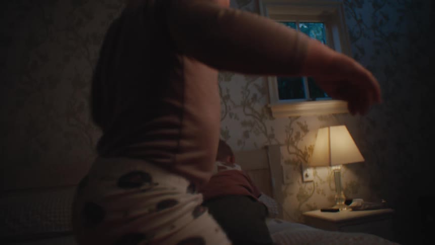 A little blonde baby girl is walking upright on a bed and a bigger little boy then jumps on the bed