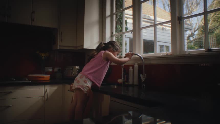 Little girl leaning on chair and brushing her teeth at kitchen sink