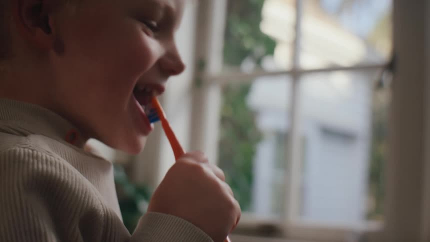 A boy brushes his teeth happily