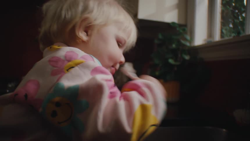 A toddler brushing her teeth at the kitchen sink at home