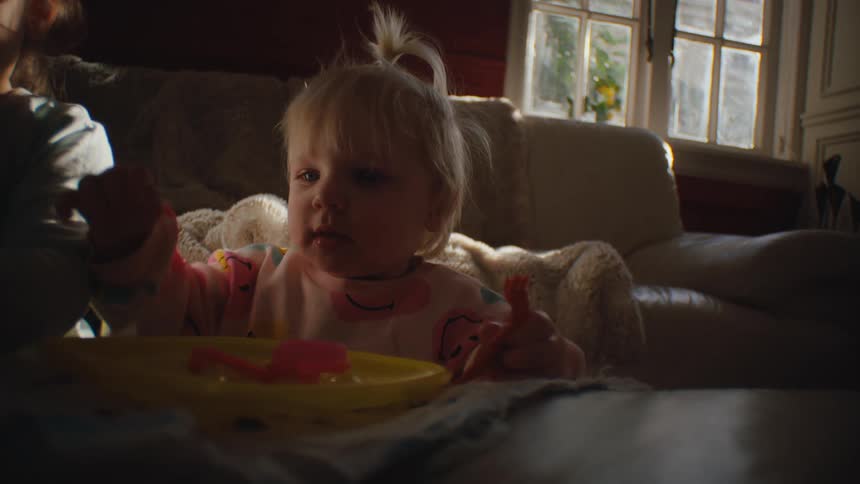A baby messily eats with her hands in the living room at home