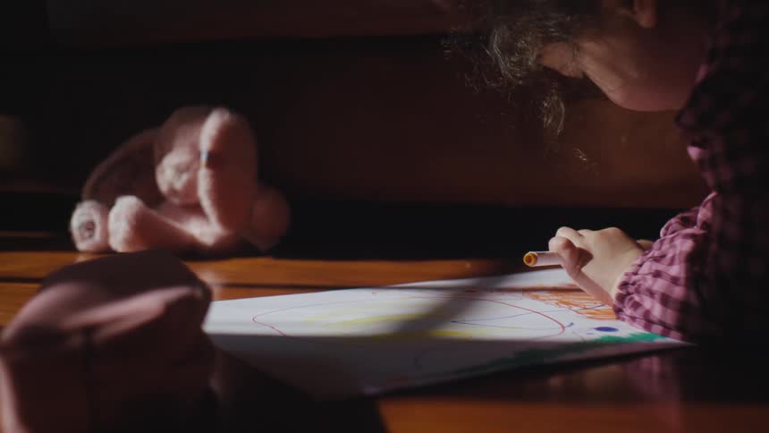 A child writing or drawing on a piece of paper at a wooden table
