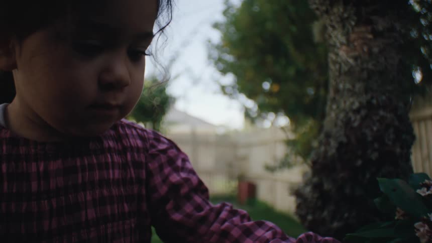 Close up of a girl picking up small flowers from the garden in the backyard