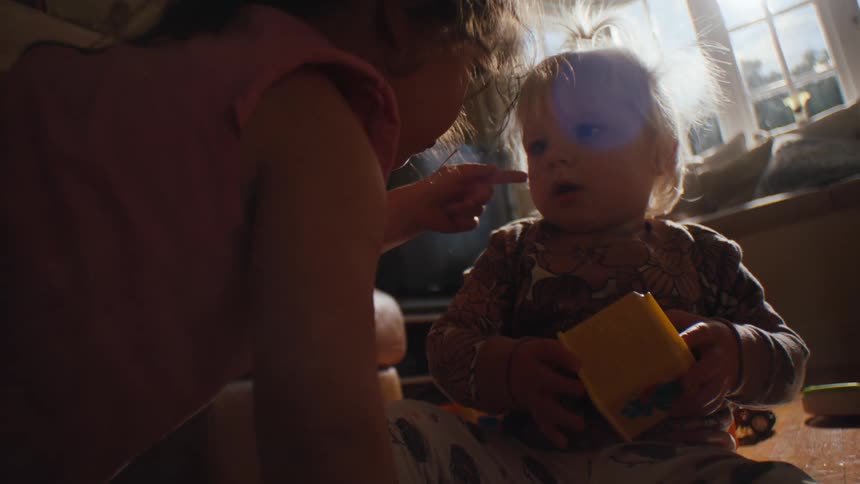 Girl touching her finger on another little girls face while they are sitting in the living room