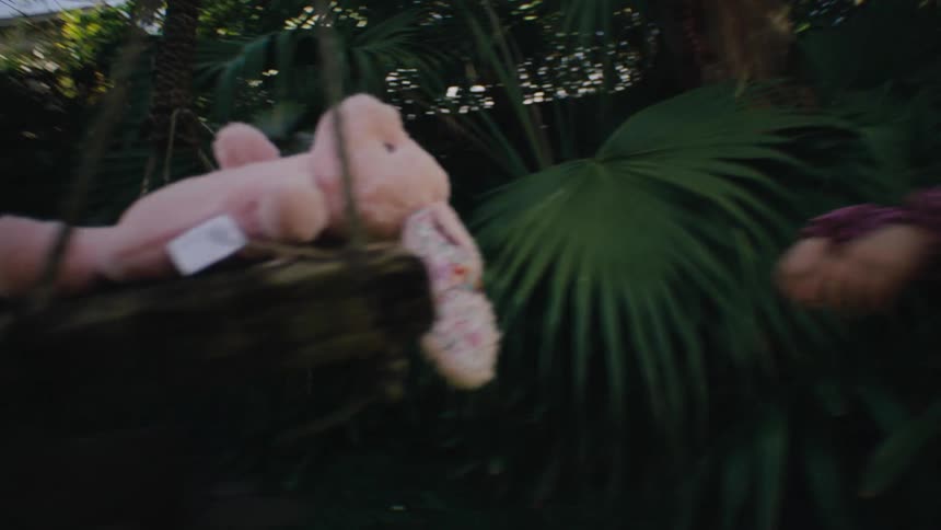 Little girl in the backyard of a house playing with a pink stuffed rabbit