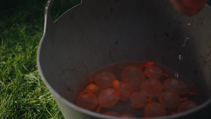A child reaches into a bucket and pulls out an orange water balloon