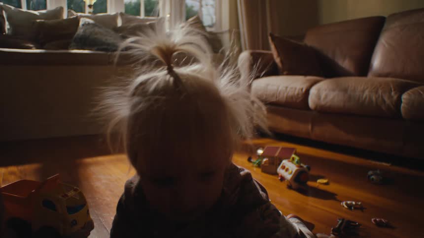 A child sitting on a wooden floor surrounded by various toys