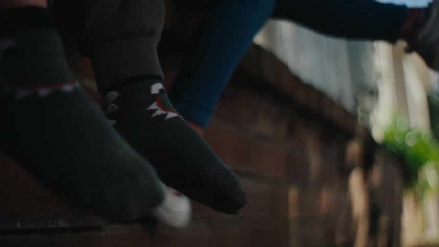The legs of a person wearing jeans and white sneakers with pink laces and they are moving their legs back and forth
