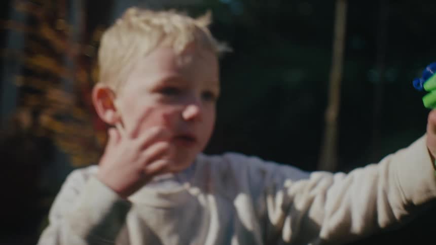 A boy runs in the backyard holding a green and orange water gun