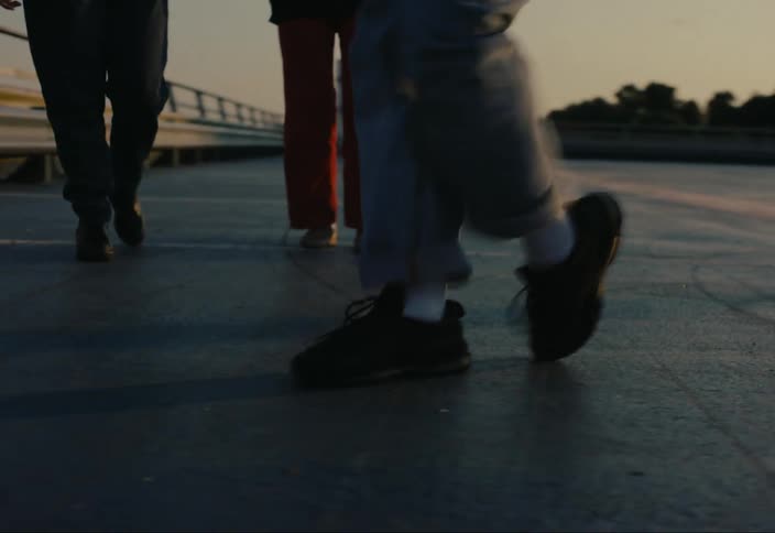The legs of a person wearing jeans and black shoes who is dancing on a smooth ground and there are some people around