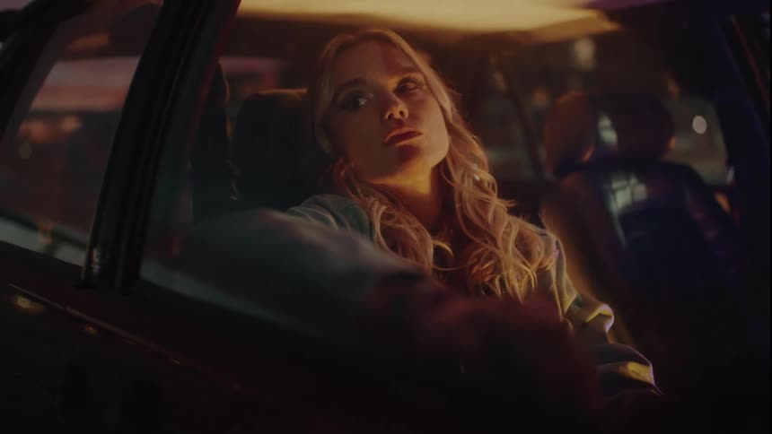 A beautiful woman reclines in the passenger seat of a car looking out the window at night