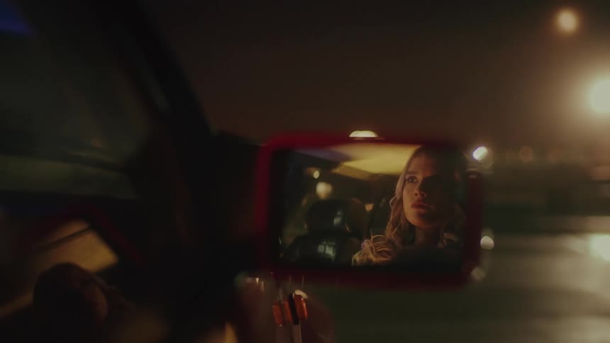 Closeup of a cars rearview mirror reflects the face of a young blonde woman