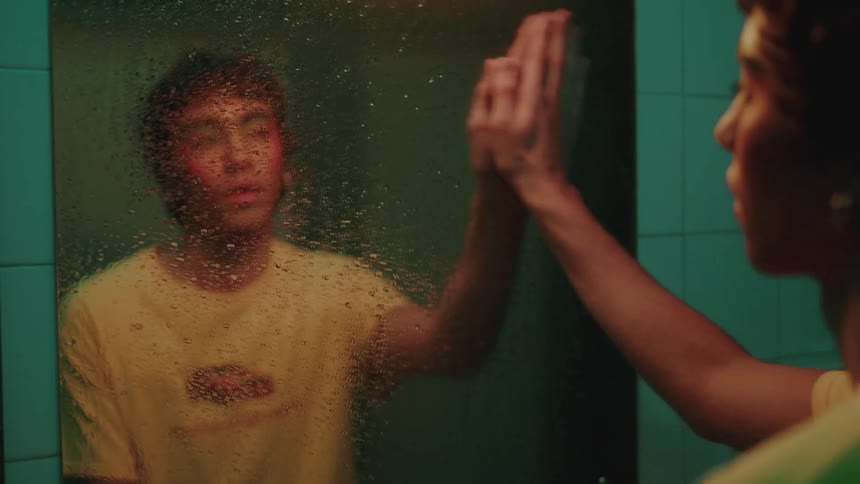 Young person in front wiping water off mirror