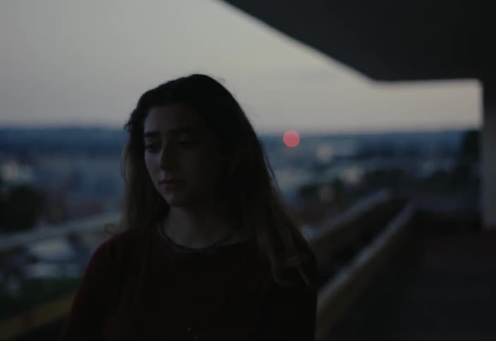 Closeup of a sad young womans face standing on a balcony in the city at dusk