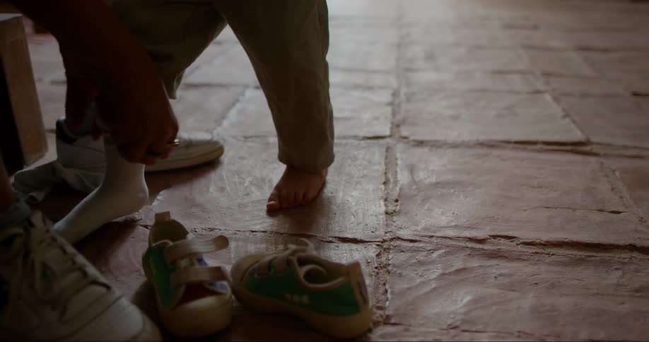 An adult helps a toddler put on socks over a tiled floor