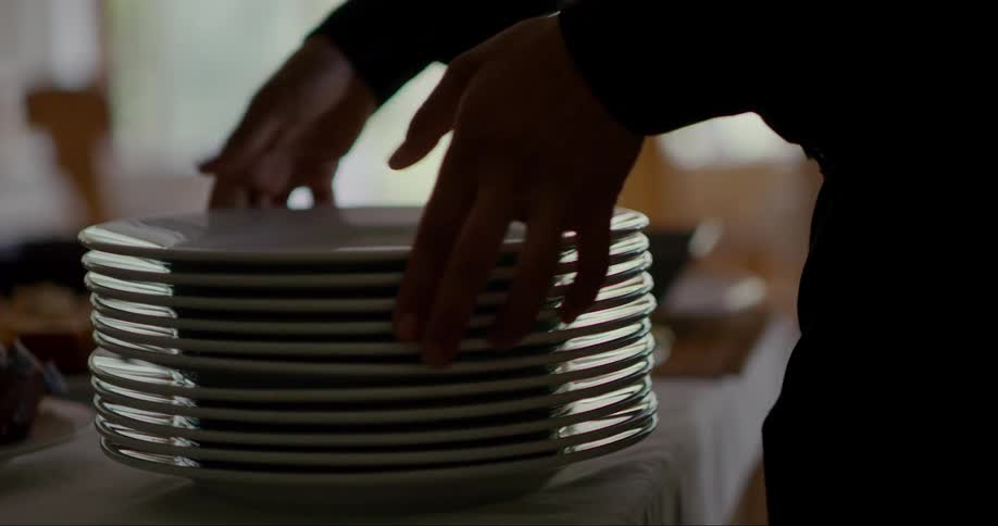 Person placing a stack of clean plates on a table