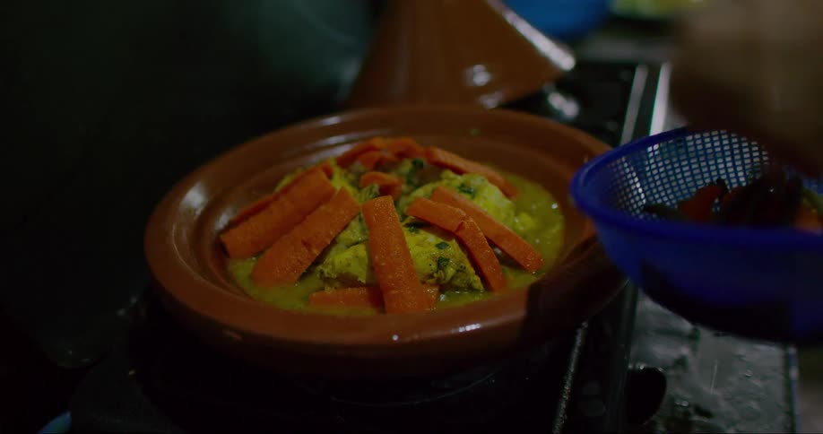 Hand placing chopped carrots in a bowl on top of the stove