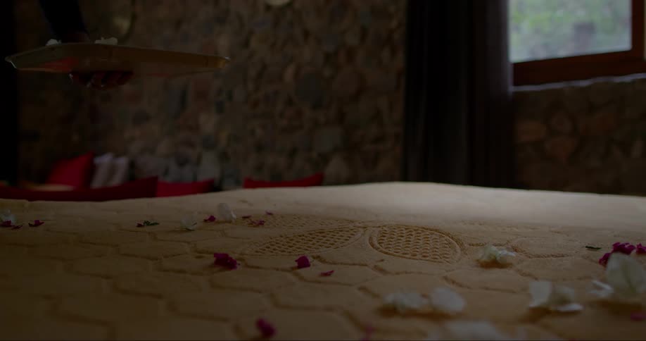 A person throws petals onto a blanket on a bed from a tray