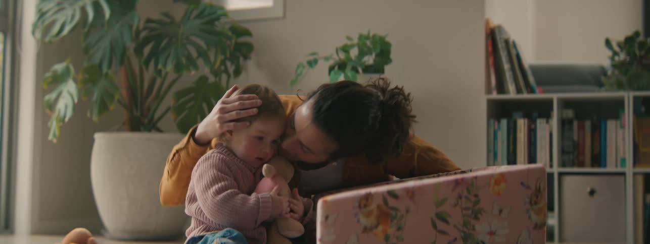 Mother next to her little daughter giving kisses and while the child interacts with the teddy bear