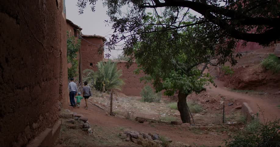A rural scene with a family walking along a dirt path between adobe buildings