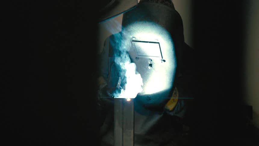 Metalworker with protective helmet welding metal and sparks coming out