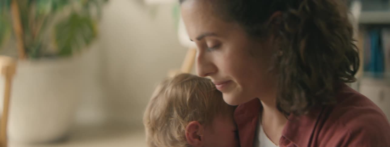 A mother picks up her toddler son while talking on her smartphone