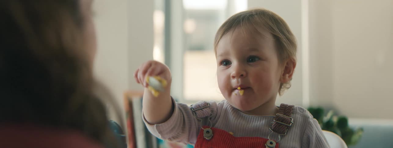 Mother watching her little daughter eating with a spoon