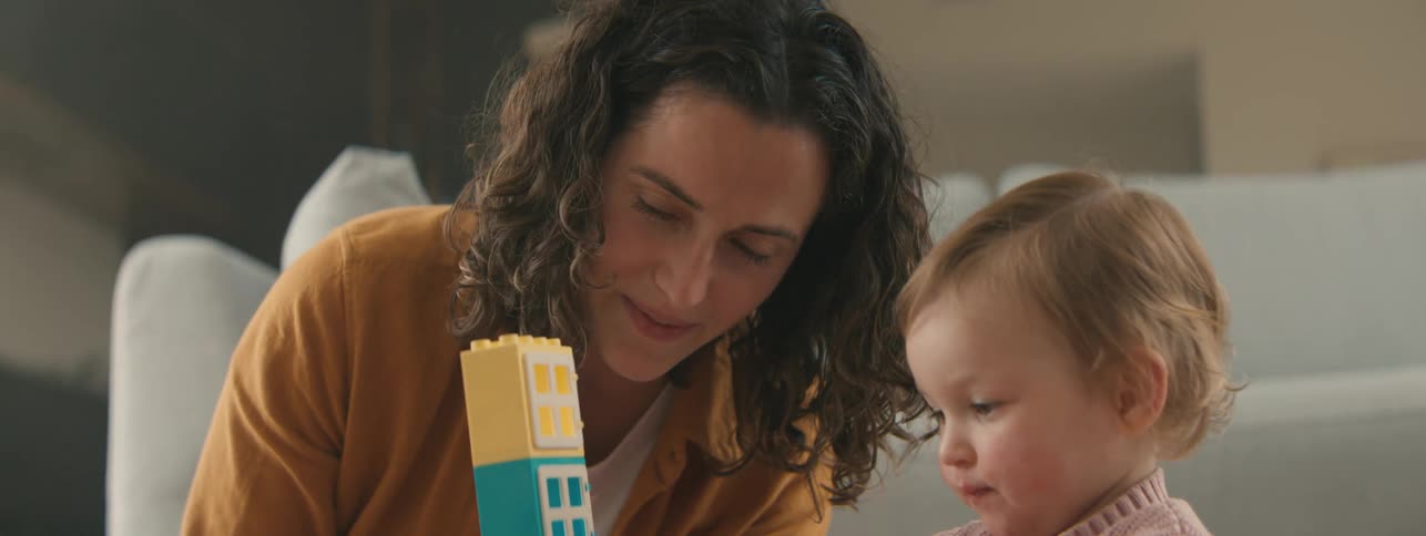 A mother and child laugh while playing with building blocks in a living room