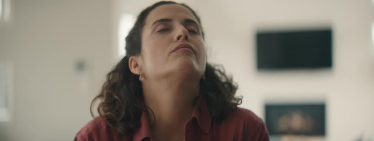 Young woman sighing and stretching her neck in living room.
