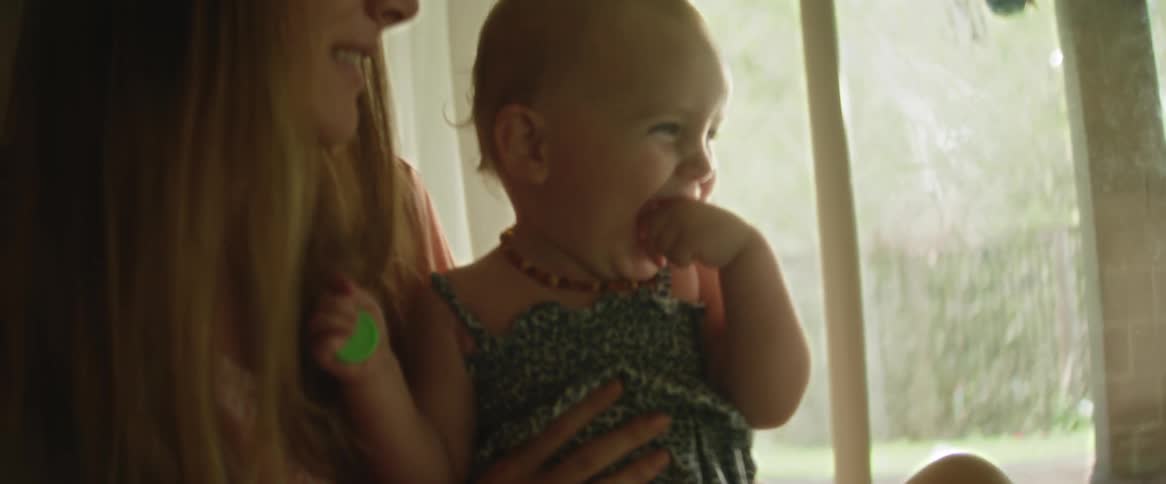 Smiling mother holds her happy daughter while sitting near a glass door