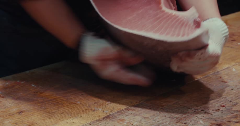 Hand with gloves cleaning a piece of salmon on a wooden table