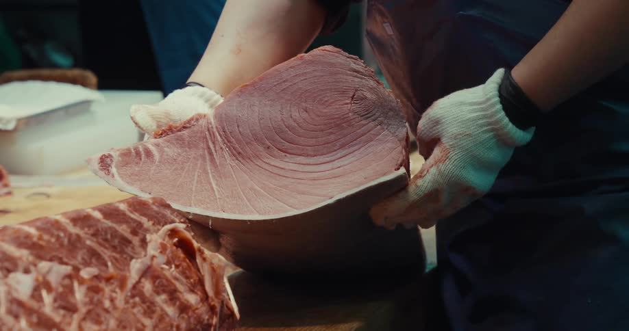 Hand with gloves picking up a cut piece of fresh tuna