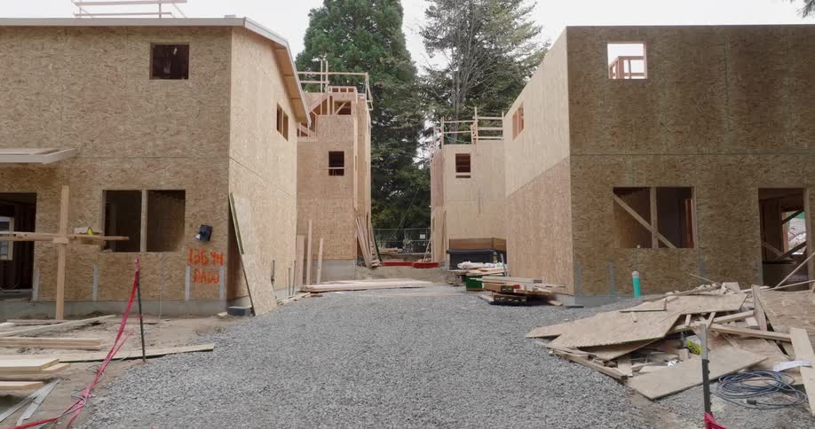Wood and other building materials stand beside new homes under construction