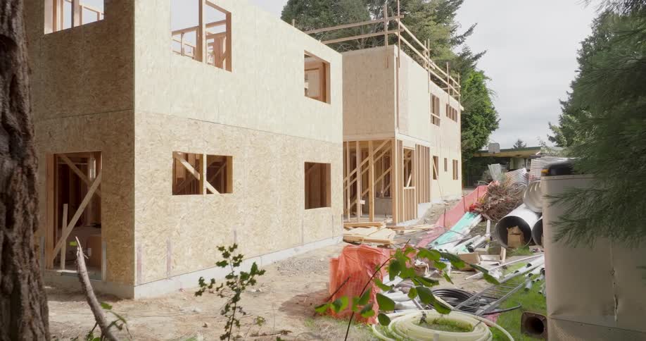 Piles of construction supplies and debris lie on the ground next to new homes under construction on a residential development