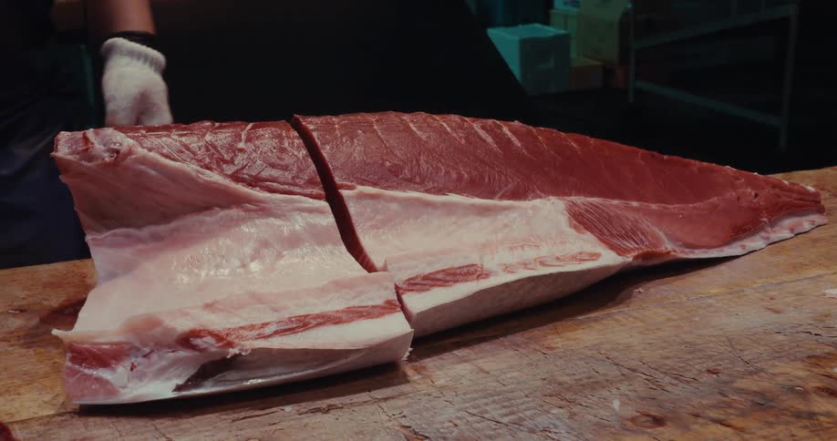 Hand with gloves cutting a piece of fresh salmon and placing it on the scale