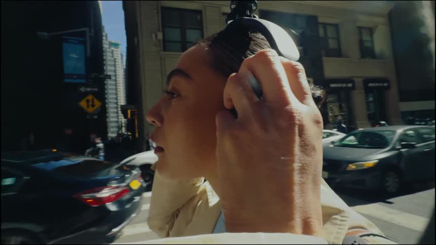 Closeup of a woman standing on a bustling city street putting on large headphones