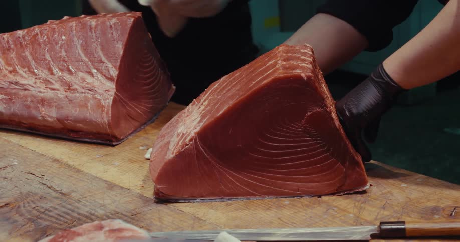 A large tuna steak being cut on a wooden cutting board