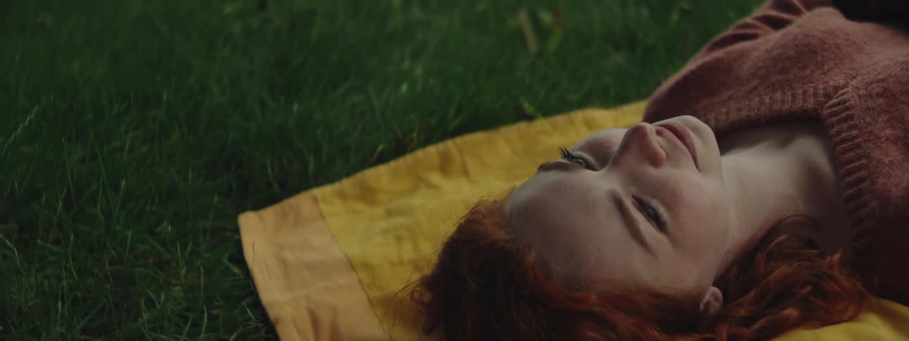 A red haired teenage girls smiles as she lies on a towel outdoors