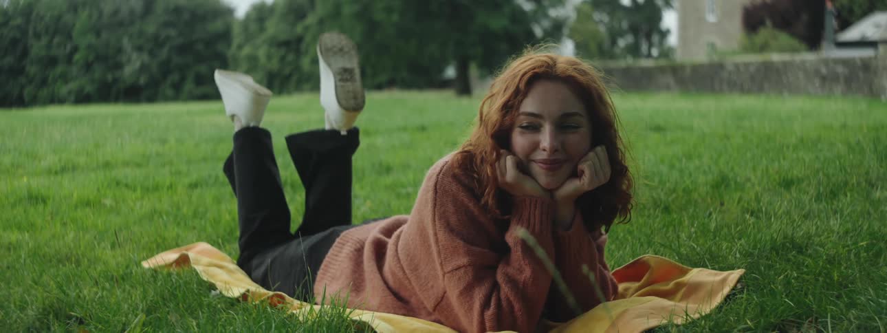 Redhead woman with happy facial expression lying on grass