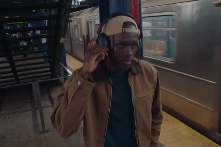 Man with headphones walking next to a train at a subway station