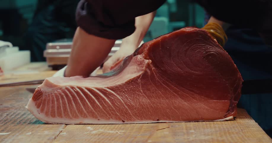 Two people cutting a piece of fresh tuna