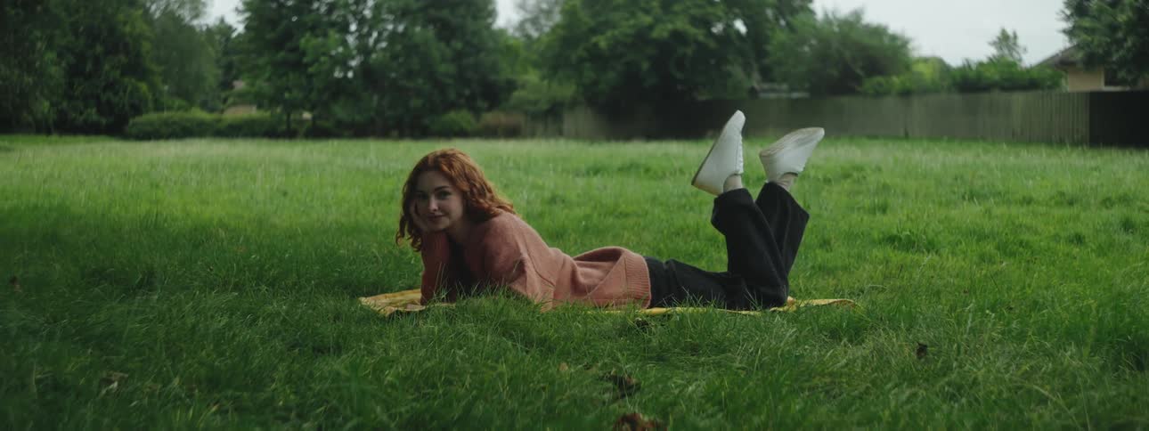 A young woman is lying on a patch of grass in a field