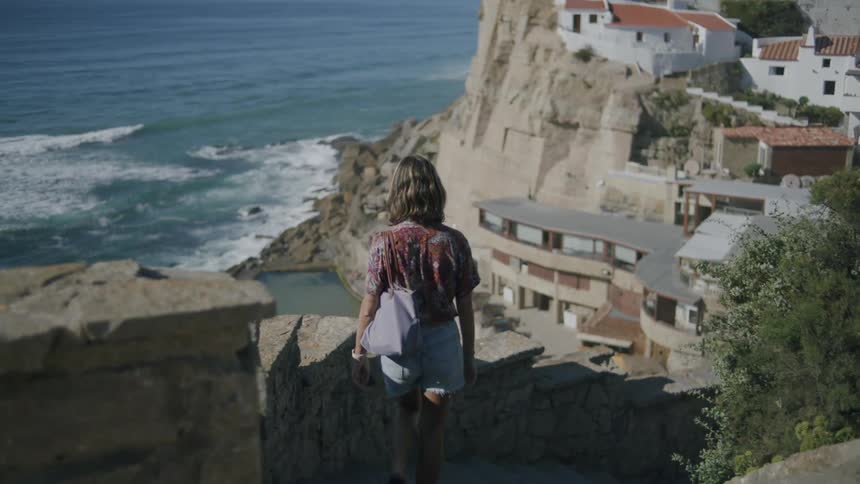 Woman seen from behind walking down the stairs of an urban neighborhood on the edge of a beach