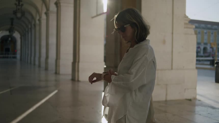 Woman in a public space between columns looking at the clock