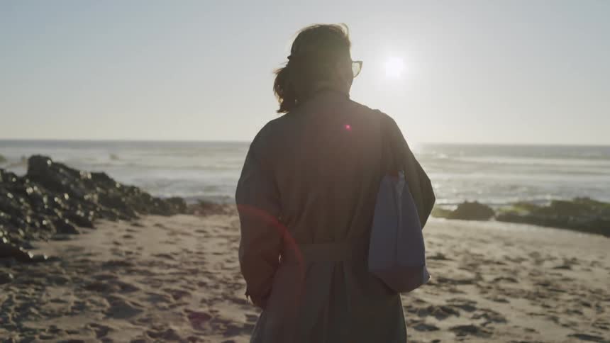 A woman in a trench coat strolls across a beach